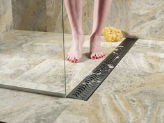 a woman's feet standing on a bathroom floor next to a shower grate