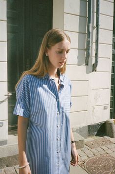 a woman standing on the sidewalk with her hand in her pocket and looking at something