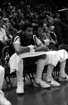 a black and white photo of a man sitting on a bench in front of a crowd