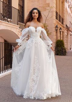 a woman in a white wedding dress standing on the street with her hands on her hips