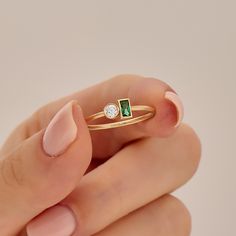 a woman's hand holding a gold ring with an emerald and diamond on it