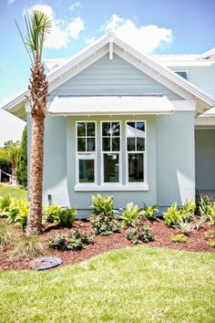 a blue house with white trim and palm tree in the front yard on a sunny day