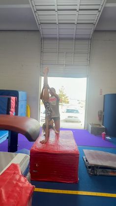 a woman standing on top of a red box in a gym area with other equipment