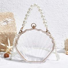 This Transparent Pearl Portable Shell Shape Bag is perfect for your vacation needs. With its chic and trendy design, you can easily carry your essentials in style. The pearl strap adds a touch of elegance, while the transparent material makes it easier to find what you need. Don't sacrifice fashion for convenience - have both with this mini portable bag. Material: Acrylic Elegant Beach Bag With Pearl Handle, Summer Beach Shoulder Bag With Clear Strap, Elegant Beach Bags With Pearl Handle, Elegant Beach Shoulder Bag With Pearl Handle, Trendy Clear Shoulder Bag For Beach, Summer Evening Bag Made Of Pearl, Trendy Clear Shoulder Bag For The Beach, Elegant Clear Travel Bag, Summer Evening Pearl Bag