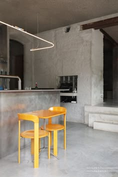 two yellow chairs sitting at a table in a room with concrete walls and flooring