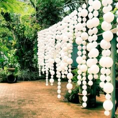 a bunch of white balls hanging from the side of a building in a garden area