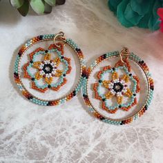 two pairs of beaded hoop earrings sitting on top of a white table next to a potted plant