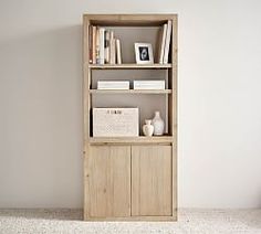 a book shelf with books and pictures on it in a white walled room, next to a window