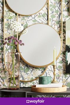 two round mirrors sitting on top of a table next to a vase with flowers in it