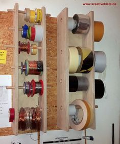 several spools of thread are stored in a wooden storage box on the wall