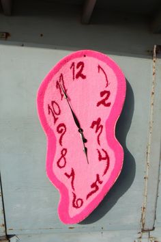 a pink clock with writing on it is hanging from the side of a metal wall