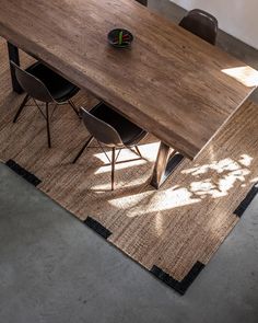 a wooden table sitting on top of a rug next to two chairs and a vase