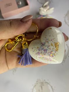 a person holding a heart shaped keychain in their left hand with glitters on it