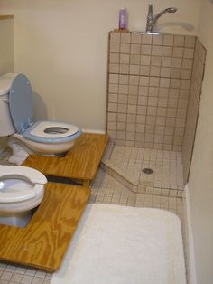 two toilets sitting in a bathroom next to each other on top of wooden platforms with their lids open