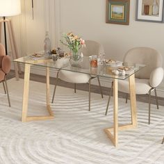 a glass table with chairs around it and a vase on the side, in front of a white rug