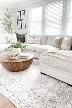 a living room with white couches and pillows on top of a rug in front of a window