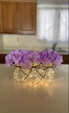 three mason jars filled with purple flowers sitting on top of a counter