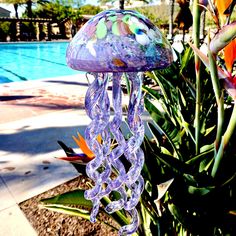 a glass jellyfish hanging from a tree next to a swimming pool