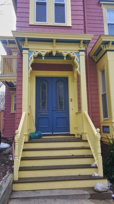 a yellow and blue house with stairs leading up to the front door that is painted pink