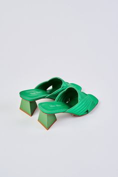 Ultra-chic, ultra-comfortable, introducing our Stella Satin Mule. Crafted from satin in brilliant metallic Green, this shoe features a trendy triangular shaped heel in a tonal shade of green. We love the chic cut-out crossover design and square-shaped peep toe. Complete your look with this bold pop of colour. Green Sandals With Sculpted Heel, Green Sandals With Sculpted Open Heel, Modern Green Open Heel Heels, Green Heels With Padded Heel, Green Open Heels With Padded Heel, Green Open Heel Heels With Padded Heel, Green Open Heel Padded Heels, Green Sandals With Sculpted Block Heel, Modern Green Heels For Summer