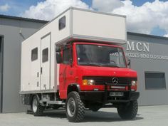 a red truck parked in front of a building with a white box on it's back