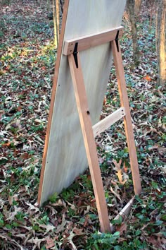 a wooden easel sitting on top of leaves in the woods