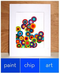 an art print of colorful circles on white paper in a square frame against a wooden wall