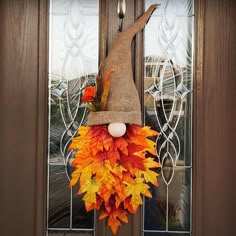 a scarecrow door hanger decorated with fall leaves and an egg in the center