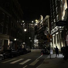 an empty city street at night with cars parked on the side and people walking down the sidewalk