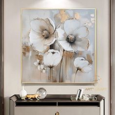 an abstract painting with white flowers on a gray wall above a black and gold dresser