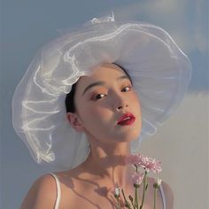 a woman wearing a white hat with flowers in front of her face and the sky behind her