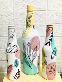 three painted vases sitting on top of a wooden table next to a white brick wall