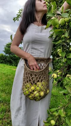 a woman standing in front of a tree holding a basket filled with apples and looking up into the sky