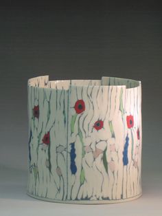 a white vase with red and blue flowers on it's side, against a gray background