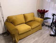 a yellow couch sitting in front of a window next to a exercise bike and table