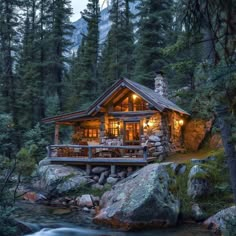 a log cabin is lit up at night in the woods near a stream and trees