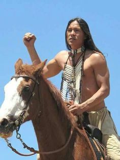 a native american man riding on the back of a brown and white horse with his fist raised