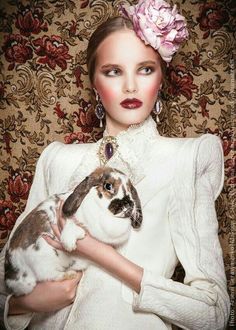 a woman holding a rabbit in her hands and wearing a white dress with pink flowers on it