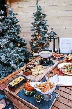 a wooden table topped with lots of food next to a christmas tree covered in lights