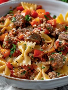 a white bowl filled with pasta and meat covered in tomatoes, parmesan cheese and herbs