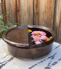 a wooden bowl filled with water and flowers on top of a white table cloth next to a wooden fence