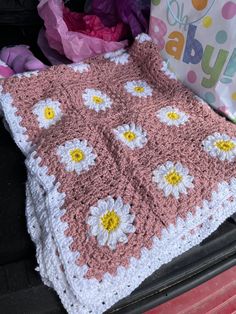 a pink and white crocheted blanket sitting on the back of a car trunk