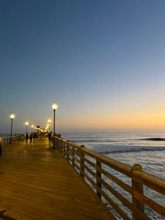 people are walking along the pier at sunset