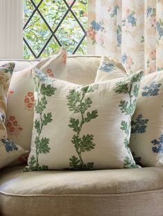 a couch with pillows on it in front of a window that has floral curtains and windowsills