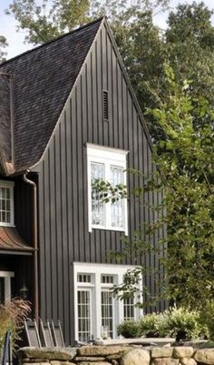 a black house with white windows and a stone wall in front of it is surrounded by trees