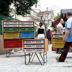 people are walking down the street with colorful crates on wheels and one man is looking at something