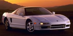 a white sports car parked in front of a mountain range at sunset with the sun setting