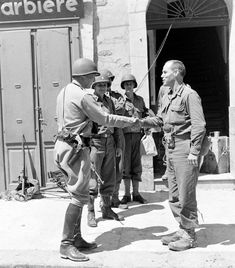 black and white photograph of men in uniform shaking hands with one another outside a building