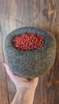 a hand holding a gray felt bowl with red flowers in it on a wooden surface