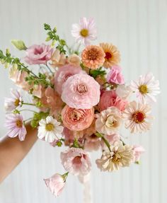 a person holding a bouquet of pink and white flowers in their hand on a table